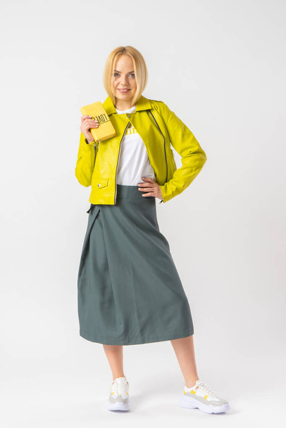 A young blonde woman in a stylish casual outfit, with a small leather clutch bag. Model posing in the studio on a white background. - Foto, Imagem