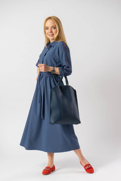A young blonde woman in an elegant casual fashionable summer dress and with a large women's bag in her hands. Model posing in the studio on a white background. - Foto, immagini