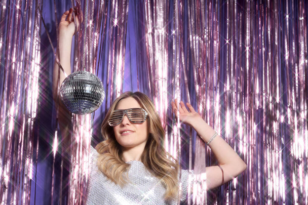 Beautiful stylish woman posing on shiny background with disco ball - Φωτογραφία, εικόνα