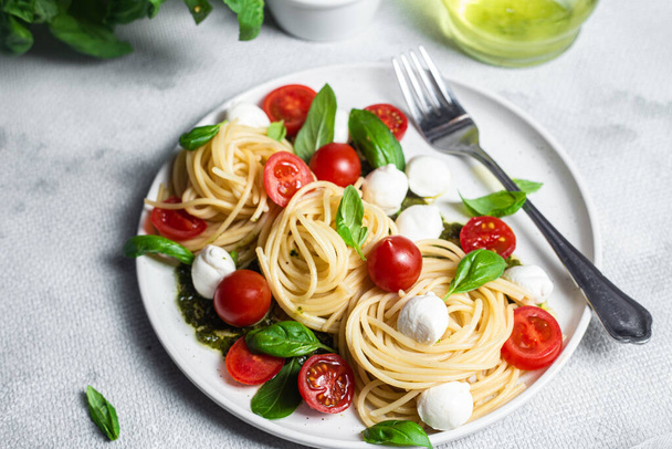 Spaghetti with mozzarella, tomatoes, basil and pesto sauce. Pasta Caprese - Foto, afbeelding