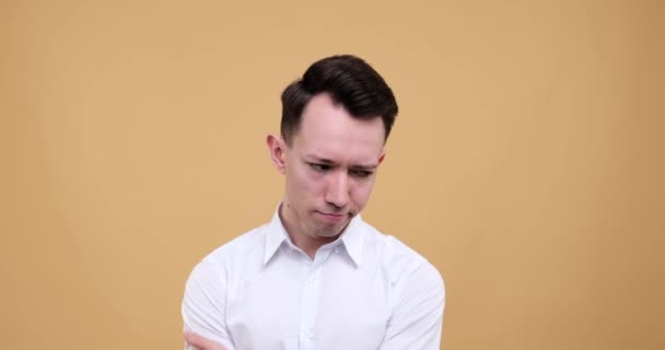 Caucasian man stands against a neutral beige background, his face etched with a sense of bewilderment. Lost in a sea of thoughts, he grapples with the complexities of decision-making. - Footage, Video