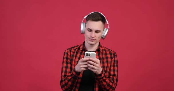Στο κόκκινο φόντο, ένας νεαρός Καυκάσιος φαίνεται να απολαμβάνει το χρόνο του με ένα τηλέφωνο στο χέρι, ενώ ακούει μουσική. Φοράει μια ικανοποιημένη έκφραση, εντελώς απορροφημένη από τη μουσική.. - Πλάνα, βίντεο