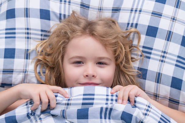 Kid in bed with comfortable mattress soft pillow white bedding. Kid wake up cover blanket. Good morning. . Childhood concept - Foto, afbeelding