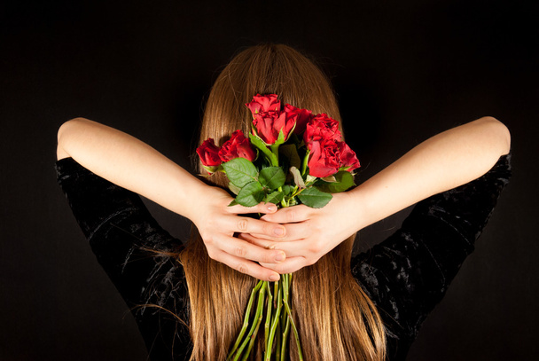 eine junge schöne Frau mit roten Rosen auf schwarzem Hintergrund - Foto, Bild