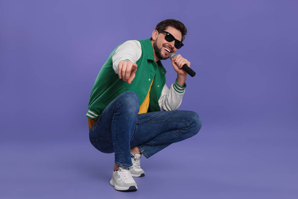 |Handsome man with sunglasses and microphone singing on purple background - Photo, image
