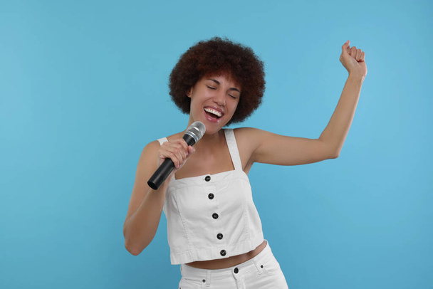 Кудрявая молодая женщина с микрофоном поет на светло-голубом фоне - Фото, изображение