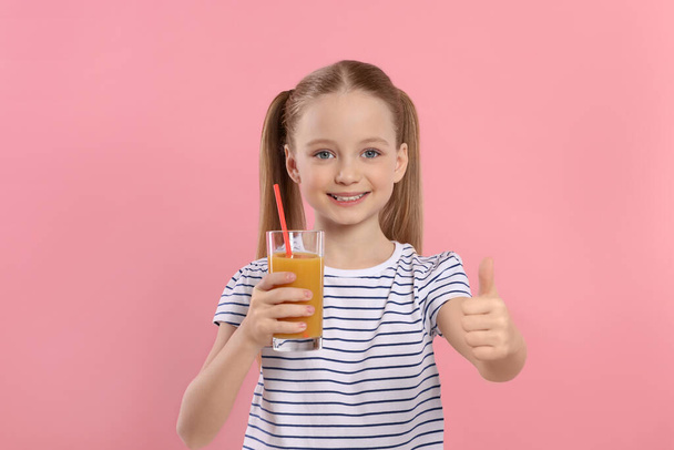 Cute little girl holding glass of fresh juice with straw and showing thumbs up on pink background - Φωτογραφία, εικόνα