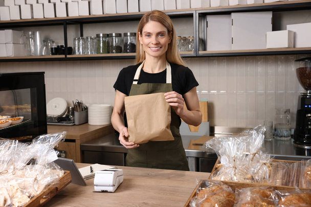 Happy seller with paper bag at cashier desk in bakery shop - Foto, Imagen