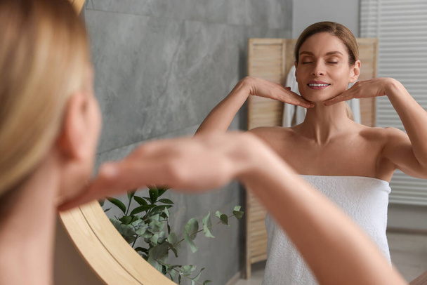 Woman massaging her face near mirror in bathroom - Zdjęcie, obraz