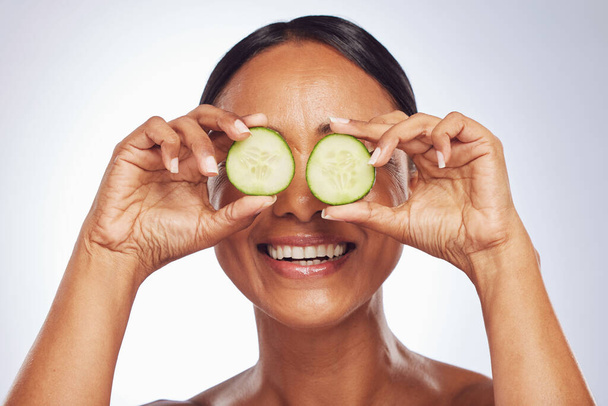 Cucumber, face and beauty of woman in studio, white background and aesthetic glow. Happy female model, natural skincare and fruits on eyes for sustainable cosmetics, vegan dermatology and nutrition. - Fotografie, Obrázek