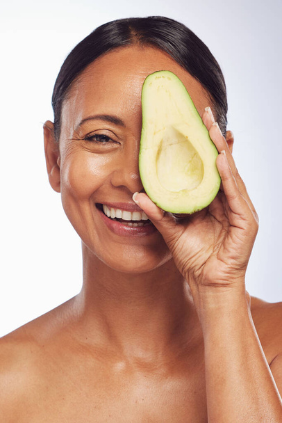 Face, skincare and senior woman with avocado in studio isolated on a white background. Happy, natural fruit or portrait of mature model with food for nutrition, healthy diet or omega 3 for anti aging. - Foto, imagen