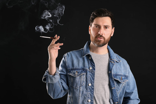 Άνδρας που χρησιμοποιεί καπνοθήκη για κάπνισμα σε μαύρο φόντο, χώρος για κείμενο - Φωτογραφία, εικόνα