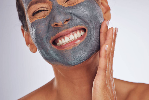 Happy woman, charcoal mask and face for beauty on studio background. Mature female model smile with clay skincare product, facial cosmetics or aesthetic makeup for dermatology, collagen and self care. - Photo, Image