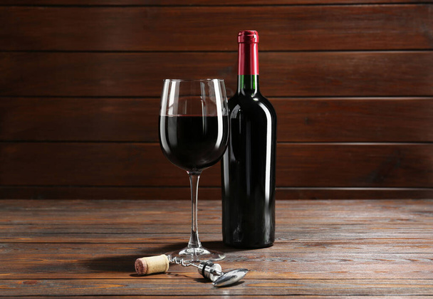 Corkscrew, glass and bottle of red wine on wooden table - Foto, imagen