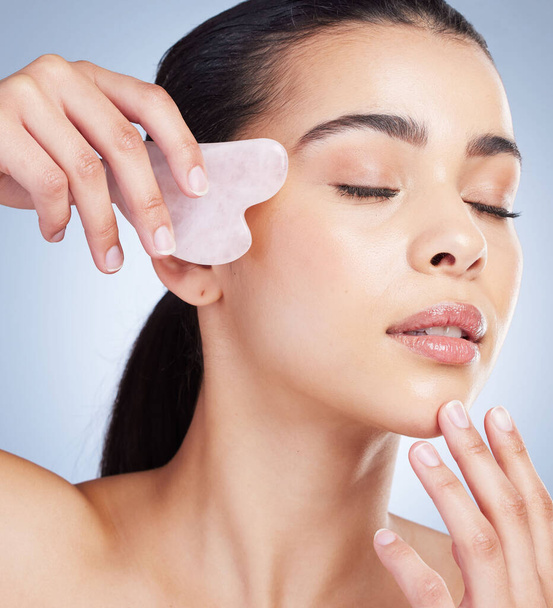 Gua sha, massage and asian woman with skincare tool in studio for anti aging, circulation or fine lines on grey background. Rose quartz, beauty and lady model with face crystal or lymphatic drainage. - Foto, Bild