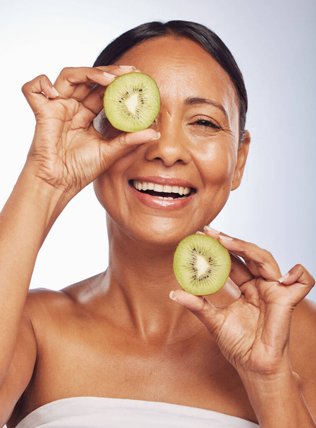 Face, skincare and senior woman with kiwi in studio isolated on a white background. Food, natural fruit and portrait of happy model with nutrition for wellness, healthy diet and anti aging for beauty. - Foto, Imagem