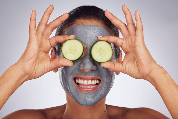 Facial, cucumber and mask with a model woman in studio on a gray background for an antiaging face treatment. Eyes, skincare and food with a happy young female person using cosmetic clay on her face. - Foto, immagini