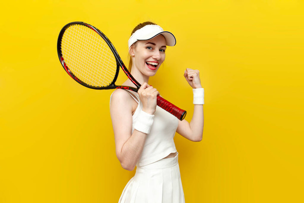 スポーツウェアの女子テニス選手の優勝者はテニスラケットを持っており、黄色の孤立した背景で勝利を喜び、白い制服の女子テニスコーチは成功と幸運を祝い、叫びます - 写真・画像