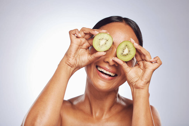Skincare, happy and senior woman with kiwi in studio isolated on a white background. Food, natural fruit and face of model with nutrition for wellness, healthy diet or vitamin c, anti aging or beauty. - Φωτογραφία, εικόνα