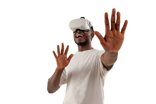 hombre afroamericano en gafas de realidad virtual toca sus manos sobre fondo blanco aislado, chico sorprendido utiliza gadget vr moderno y muestra sus palmas - Foto, Imagen