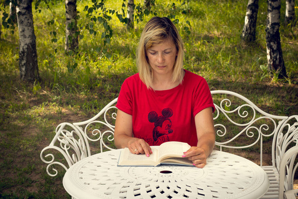 Kobieta z książką przy stole. Kobieta czyta książkę. Uczenie się na odległość w domu - Zdjęcie, obraz