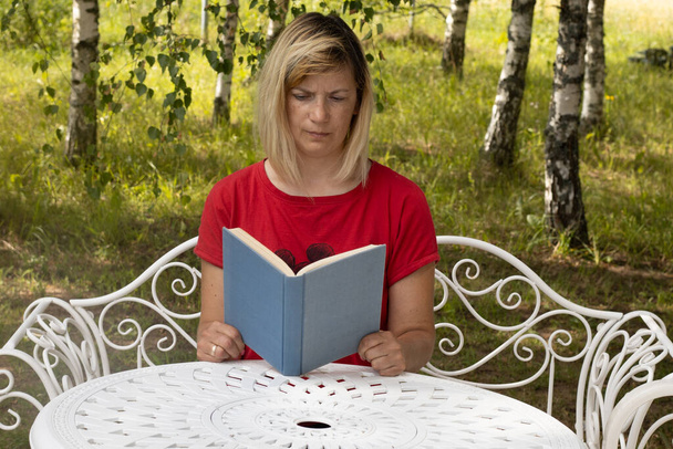 A woman with a book at the table. A woman is reading a book. Distance learning at home - Photo, Image