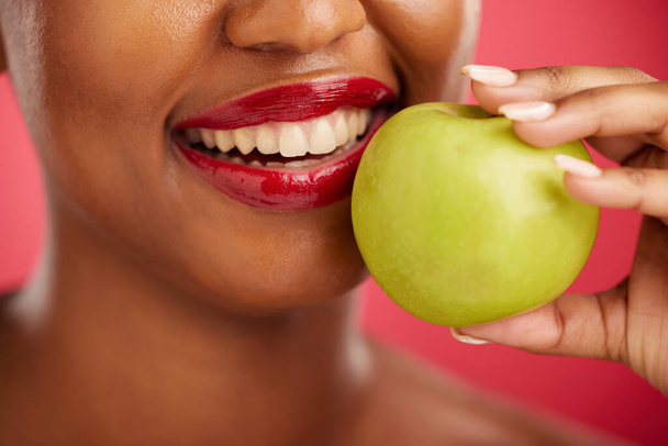 Woman, mouth and apple for natural nutrition, diet or health and wellness against a red studio background. Closeup of female person smile with lipstick and organic fruit for vitamin, fiber or food. - Foto, afbeelding