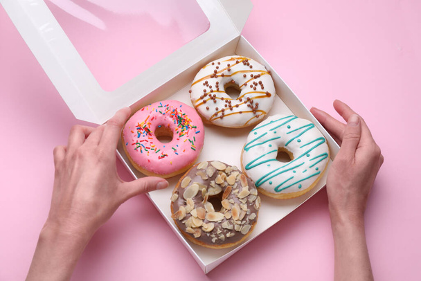 Woman taking tasty glazed donut from box on pink background, top view - Zdjęcie, obraz