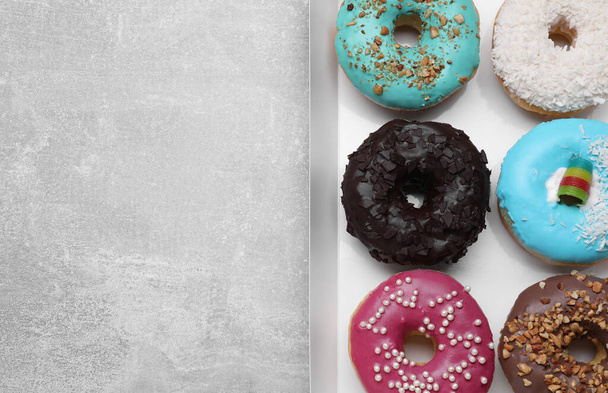 Box with different tasty glazed donuts on light grey table, top view. Space for text - 写真・画像
