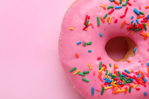 Tasty glazed donut decorated with sprinkles on pink background, closeup. Space for text - Φωτογραφία, εικόνα