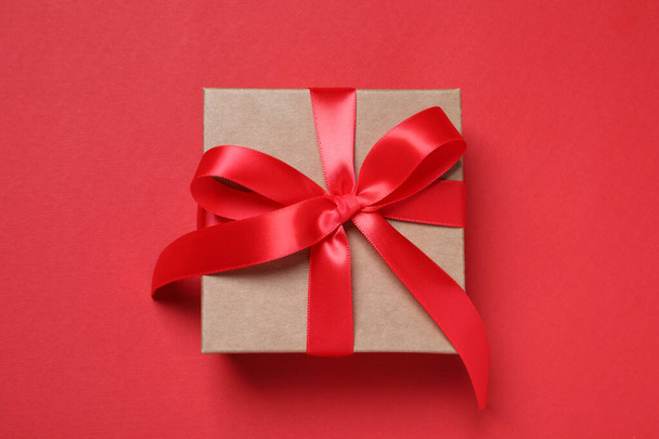 Beautiful gift box with bow on red background, top view - Zdjęcie, obraz