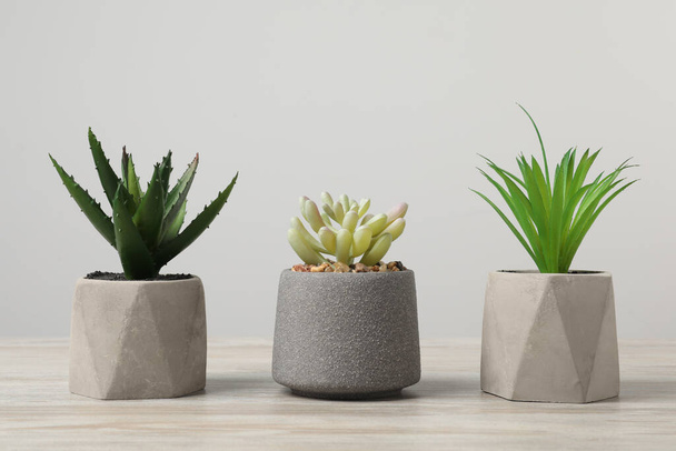 Many different artificial plants in flower pots on wooden table against light grey background - Foto, Imagem