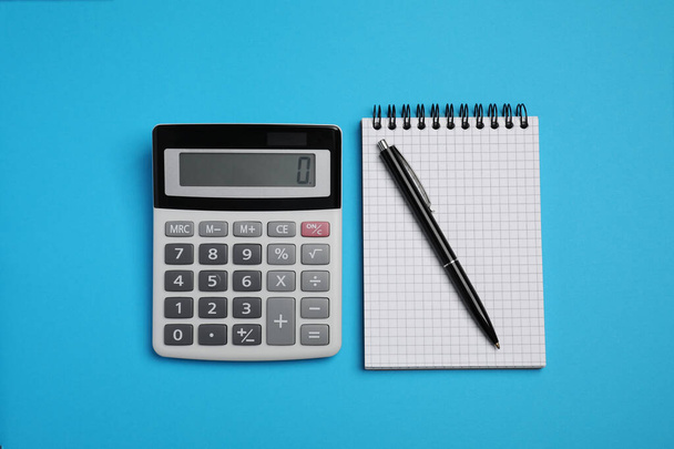 Calculator, notebook and pen on light blue background, flat lay - Фото, изображение