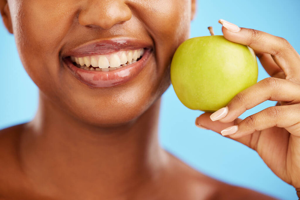 Frau, Lächeln und Apfel für Ernährung, Gesundheit und Wellness vor blauem Studiohintergrund. Nahaufnahme des weiblichen Mundraums mit natürlichen Bio-Früchten für Vitamin, Ballaststoffe oder Snacks. - Foto, Bild