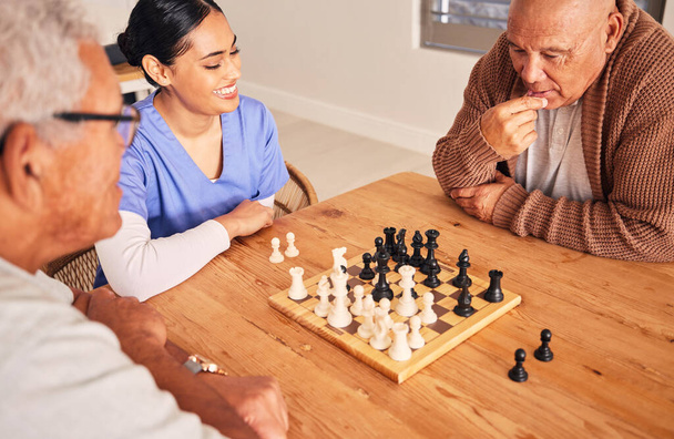 Retirement, playing and chess with senior men at nursing home for fun activity in home with nurse at table. Strategy, chessboard and challenge with elderly friends together on table for bonding - 写真・画像