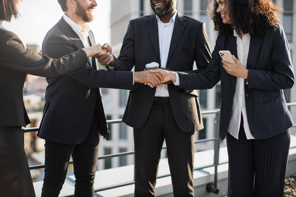 Crop of stylish corporate partners in trendy business suits shaking hands and agreeing about further cooperation. Multiethnic specialists feeling content and thanking each other for efficient meeting. - Фото, зображення