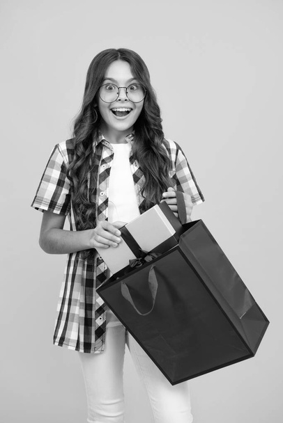 Child girl hold shopping bag enjoying sale isolated on yellow background. Portrait of teenager girl is ready to go shopping - 写真・画像