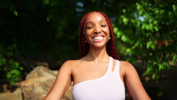 Venkovní portrét přírodní Krásná mladá Afroameričanka červené copánky účes, perfektní bílé zuby úsměv, smích zavírání fotoaparát s rukama na slunné letní den se zeleným listoví pozadí - Záběry, video