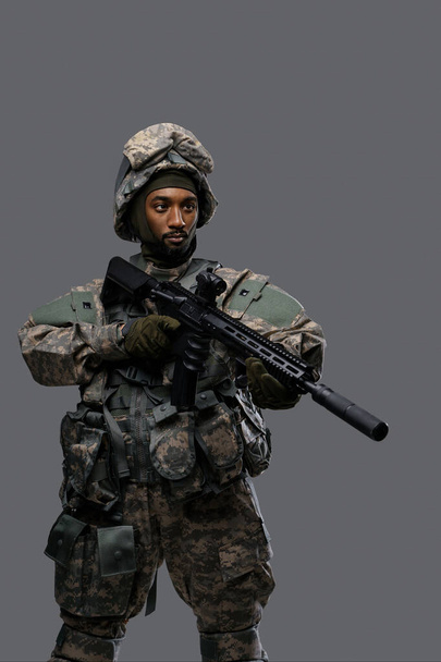 Rohkea sotilas NATOn univormussaan ja kypärässään seisoo kiväärillään, keskittyen kohteeseen, osoittaen rohkeutta - Valokuva, kuva