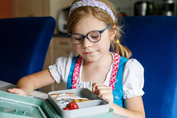 Χαριτωμένο κοριτσάκι με γυαλιά ηλίου τρώει σάντουιτς και φρούτα κατά τη διάρκεια του διαλείμματος μεταξύ των μαθημάτων. Υγιείς ανθυγιεινές τροφές για παιδιά. Πρωινό Γεύμα Κουτί για παιδιά στο σχολείο - Φωτογραφία, εικόνα
