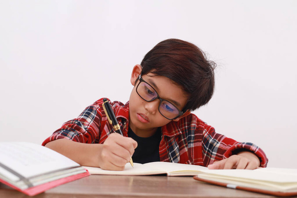 Nahaufnahme eines asiatischen Studenten, der hart auf dem Schreibtisch studiert. Isoliert auf Weiß - Foto, Bild