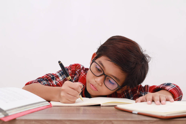 Close up foto de estudante asiático feliz estudando enquanto escrevendo algo no livro - Foto, Imagem