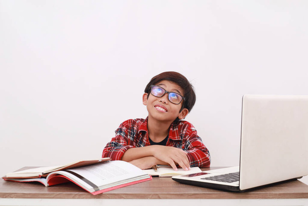 Szczęśliwy azjatycki student patrząc obrazowanie coś podczas nauki na biurku. Odizolowane na biało - Zdjęcie, obraz