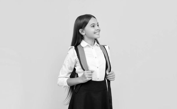 lächelnde Teenie-Mädchen tragen Rucksack. zurück zur Schule. Wissenstag. Konzept der Bildung. Kind mit langen Haaren in Uniform auf gelbem Hintergrund. 1. glückliche Kindheit. Kind mit Schultasche. - Foto, Bild