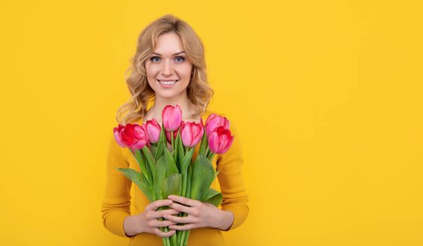 glad young girl with spring tulip flowers on yellow background. - Foto, Imagem