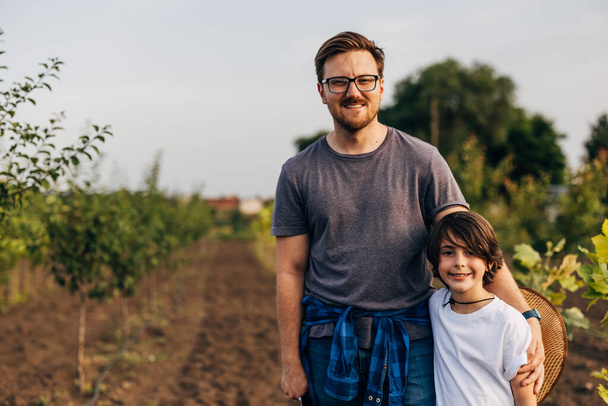 Front view of father and son standing in the orchard amongst young trees. - Foto, afbeelding