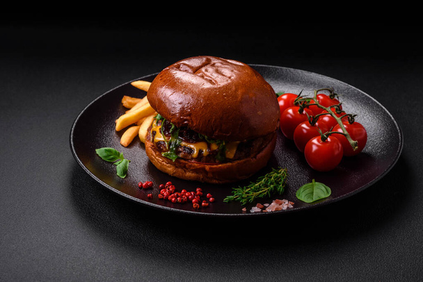 Hambúrguer com costeleta de carne suculenta, queijo, tomate, sal, especiarias e ervas em um fundo de concreto escuro - Foto, Imagem