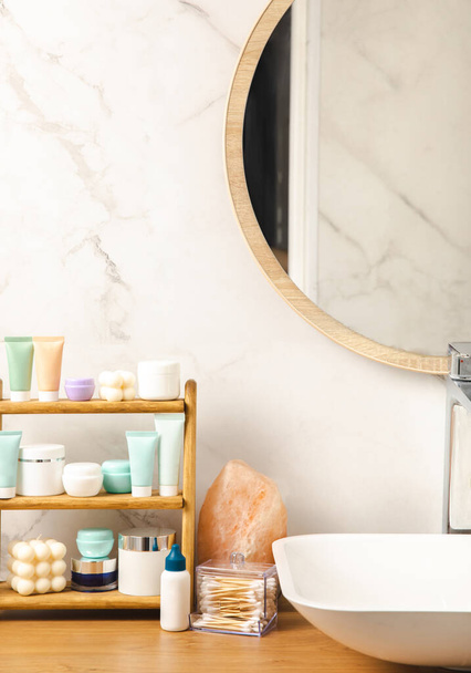Care cosmetics on the shelf in the bathroom. Cosmetic tube. Cleanser, face and body cream, face roller and gua sha, tonic. Shelf with cosmetics in the interior of the bathroom.Beauty concept.  - 写真・画像