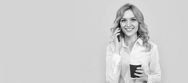 femme blonde souriante avec tasse de café parlant au téléphone sur fond jaune. Portrait de femme isolé, bannière avec maquette d'espace de copie - Photo, image