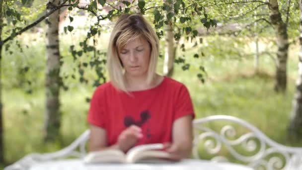 Μια γυναίκα με ένα βιβλίο στο τραπέζι. Μια γυναίκα διαβάζει ένα βιβλίο. Εκμάθηση εξ αποστάσεως στο σπίτι - Πλάνα, βίντεο